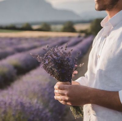 Mann im Lavendelfeld zur Unterstützung von Yoni-Steaming-Anwendungen Mann, der in einem Lavendelfeld steht; Lavendel wirkt mit seinen ätherischen Ölen antibakteriell und entzündungshemmend, ideal für Yoni-Steaming.